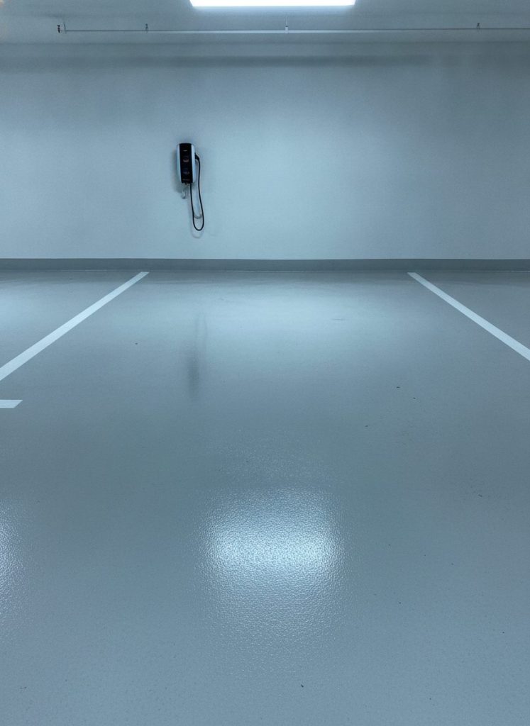 Cadrage vertical sur une place de parking de direction fraîchement nettoyée, marquage blanc franc, borne de recharge électrique au mur, béton clair sans trace, reflets nets des luminaires. Lumière artificielle froide, photoréaliste, aucun texte incrusté.